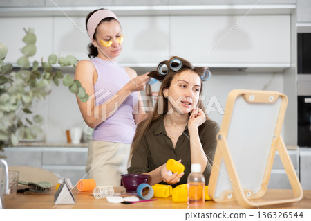 Woman applying hair rollers to friend in front to vanity mirror Woman applying hair rollers to friend in front to vanity mirror 136326544