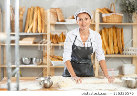 Woman works as baker in bakery, molds pies from dough, creates croissants from dough. 136326576