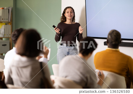 Young woman teacher gives lecture to group in lecture hall Young woman teacher gives lecture to group in lecture hall 136326580