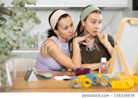 Two adult besties inspecting faces in mirror in cozy home Two adult besties inspecting faces in mirror in cozy home 136326636
