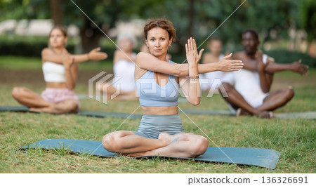 Woman stretching in lotus position during group yoga in park Woman stretching in lotus position during group yoga in park 136326691