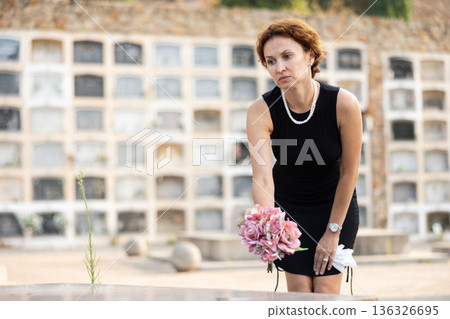 Sorrowful woman puts bouquet of hydrangeas on grave of deceased friend, mourns loss 136326695