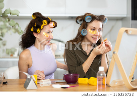 Female friends in curlers using under-eye patches during self-care routine Female friends in curlers using under-eye patches during self-care routine 136326728