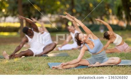 Woman performing Parivrtta Janu Sirsasana during group yoga class in park 136326892