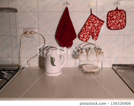 a white electric kettle and a stand with cups on a kitchen countertop near the wall 136326906