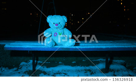 teddy bear sitting on a long bench on a winter night 136326918