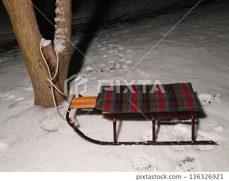wooden sled tied with a rope to a tree trunk on the snow 136326921