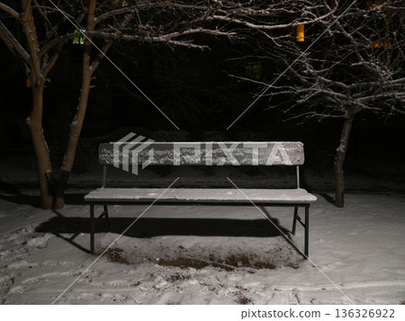 empty wooden bench covered with frost and snow in the night park 136326922