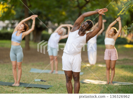 Fitness, sport and healthy lifestyle concept: group of multinational people doing yoga yoga pose - vrikshasana pose on mat in park 136326962