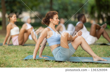 Multinational yoga enthusiasts with female coach perform hindolasana in park Multinational yoga enthusiasts with female coach perform hindolasana in park 136326994