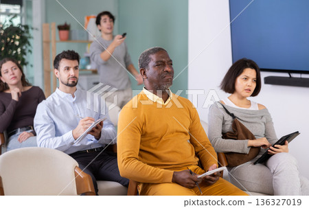 Students of different ages listen attentively to teacher and take notes in notebooks during a lecture at the learning center. Language course 136327019