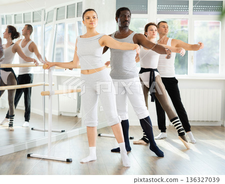 Asian woman performing battement tendu at ballet barre at group class 136327039