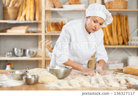 Female employee cooks croissants, rolls dough into tube, forms muffin from raw dough material Female employee cooks croissants, rolls dough into tube, forms muffin from raw dough material 136327117