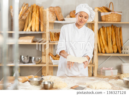 Woman works as baker in bakery, molds pies from dough, creates croissants from dough. 136327128