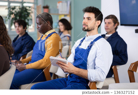 Young man worker listens and takes notes in lecture hall Young man worker listens and takes notes in lecture hall 136327152