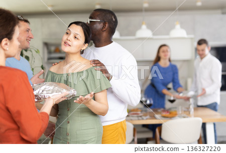 Happy middle-aged pair welcoming their guests who hand over prepared meal Happy middle-aged pair welcoming their guests who hand over prepared meal 136327220