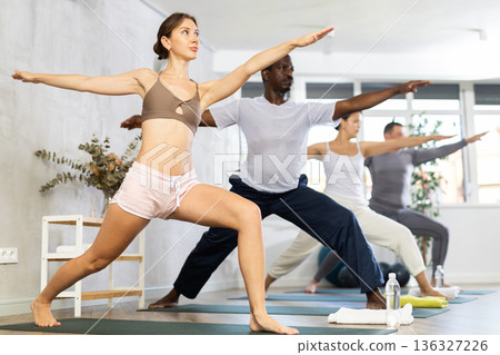 Young woman performing Virabhadrasana during group yoga class 136327226