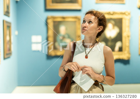 Thoughtful attentive woman standing in front of painting in art museum 136327280