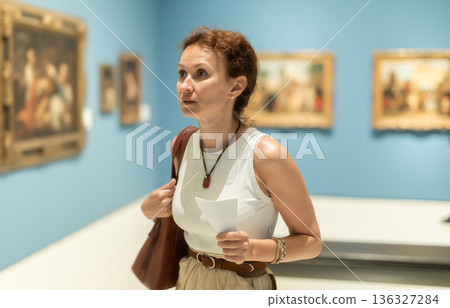 Woman viewing art gallery with brochure Woman viewing art gallery with brochure 136327284