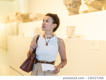Woman looking at antique museum exhibit with brochure 136327288