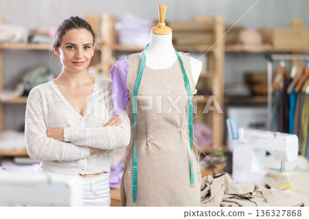 Female dressmaker standing next to mannequin in sewing studio Female dressmaker standing next to mannequin in sewing studio 136327868