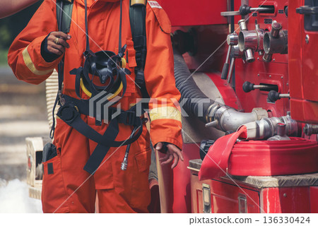 Fireman prepare equipment fighting extinguisher at fire engine truck. Firefighter fighting with smoke flame using fire hose, tube, chemical water foam spray at truck. Fireman wear hard hat protection Fireman prepare equipment fighting extinguisher at fire engine truck. Firefighter fighting with smoke flame using fire hose, tube, chemical water foam spray at truck. Fireman wear hard hat protection 136330424