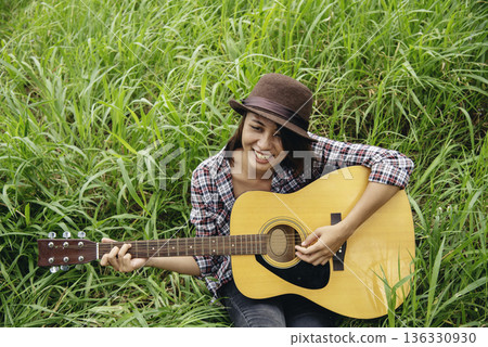 Young women playing acoustic guitar outdoor in green park. Woman person playing acoustic guitar music instrument at home, young Asian musician girl lifestyle in beautiful nature. Happy guitarist 136330930