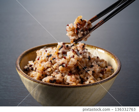 Chopsticks are used to lift a bowl of mixed grain rice placed on a table against a black background 136332763