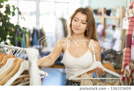 Young woman chooses dresses and tops in store 136333609