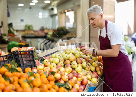 Young guy seller puts apples in vegetable shop Young guy seller puts apples in vegetable shop 136333628
