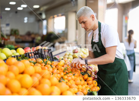 Working in supermarket - male salesman sorts through ripe tangerines on display case Working in supermarket - male salesman sorts through ripe tangerines on display case 136333670