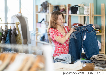 Positive young girl choosing jeans pantaloons in clothing store Positive young girl choosing jeans pantaloons in clothing store 136333710