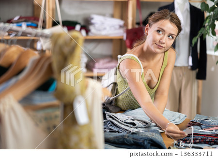 woman stands in a store near a shelf with jeans 136333711