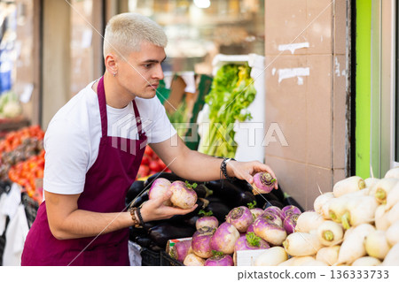Young guy seller puts turnips in vegetable shop Young guy seller puts turnips in vegetable shop 136333733