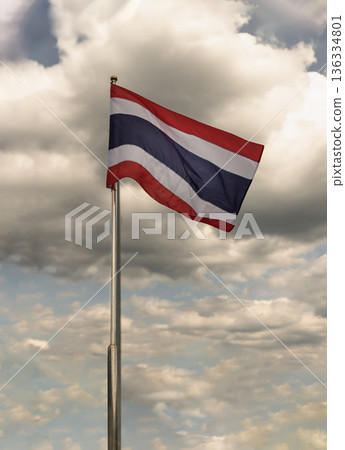 Against a backdrop of natural scenery and a vast sky, the Thai flag waves gracefully in the wind, a vibrant symbol of national pride. 136334801