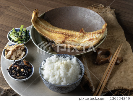 Presented alongside white rice, several small side dishes, and chopsticks, a large, golden-brown charcoal-grilled Atka mackerel (Shima Hokke). 136334849