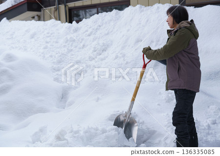 一位婦女在厚厚的雪地裡拿著鏟子不知所措。 136335085