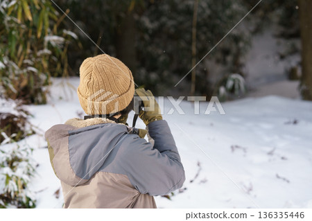 Rear view of a woman looking through binoculars outdoors in winter Rear view of a woman looking through binoculars outdoors in winter 136335446