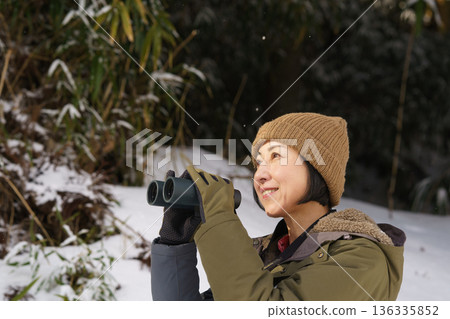 Woman looking through binoculars outdoors in winter Woman looking through binoculars outdoors in winter 136335852