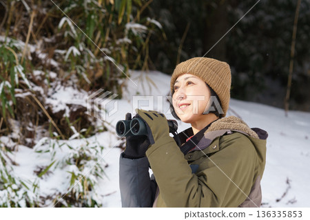 Woman looking through binoculars outdoors in winter Woman looking through binoculars outdoors in winter 136335853