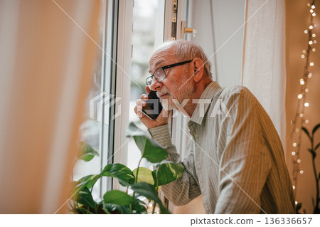 Old man making phone call, looking out of window. Old man making phone call, looking out of window. 136336657