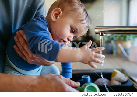 Father caring for toddler son while doing household chores. Father caring for toddler son while doing household chores. 136336794