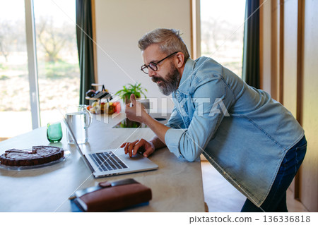 Man working from home office, drinking coffe and working on laptop. 136336818