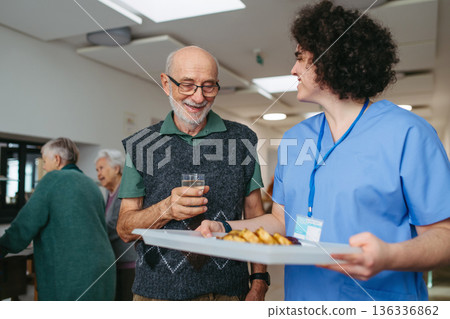Senior man having lunch with supportive caregiver in community center cafeteria. Senior man having lunch with supportive caregiver in community center cafeteria. 136336862