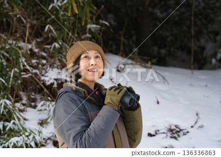 Woman looking through binoculars outdoors in winter Woman looking through binoculars outdoors in winter 136336863