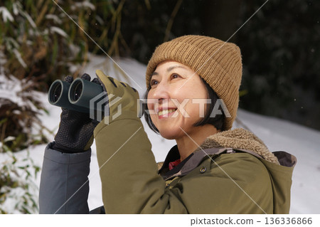 Woman looking through binoculars outdoors in winter Woman looking through binoculars outdoors in winter 136336866