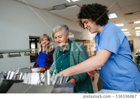 Caregiver helping older woman in community center cafeteria. 136336867