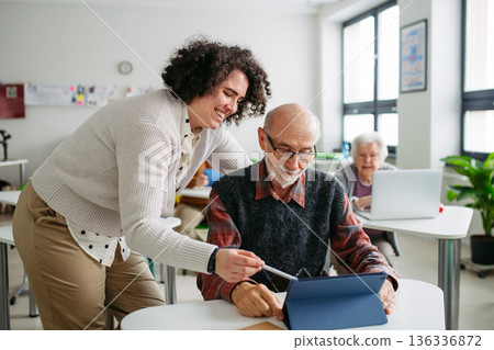 Female tutor helping senior man to learn digital skills. Female tutor helping senior man to learn digital skills. 136336872