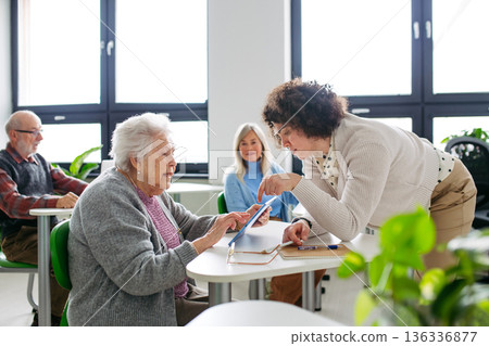 Teacher helping old woman to learn digital skills. Teacher helping old woman to learn digital skills. 136336877