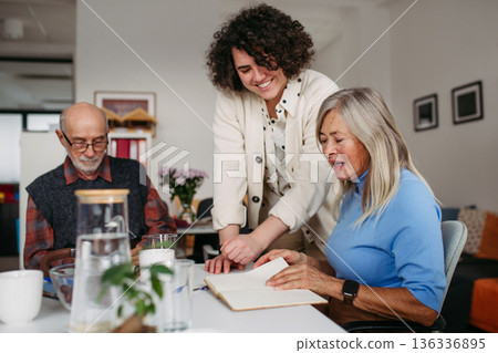 Female volunteer spending time with seniors in community center. Female volunteer spending time with seniors in community center. 136336895